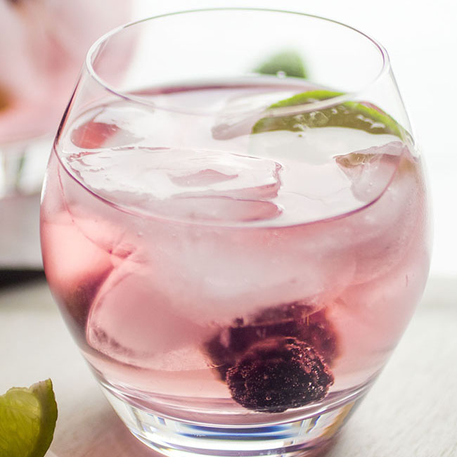 Light pink cocktail in a glass with fresh berries and a lime wedge.