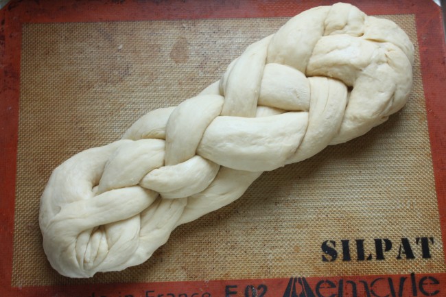 Braided challah dough on a baking sheet.