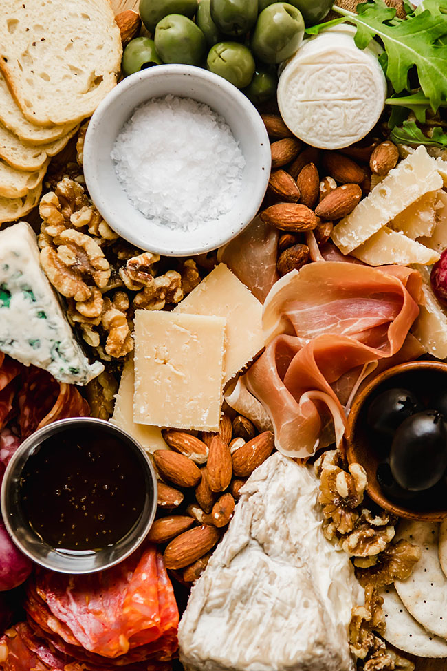 Close up of a cheese plate filled with nuts, cheeses, charcuterie, and olives.