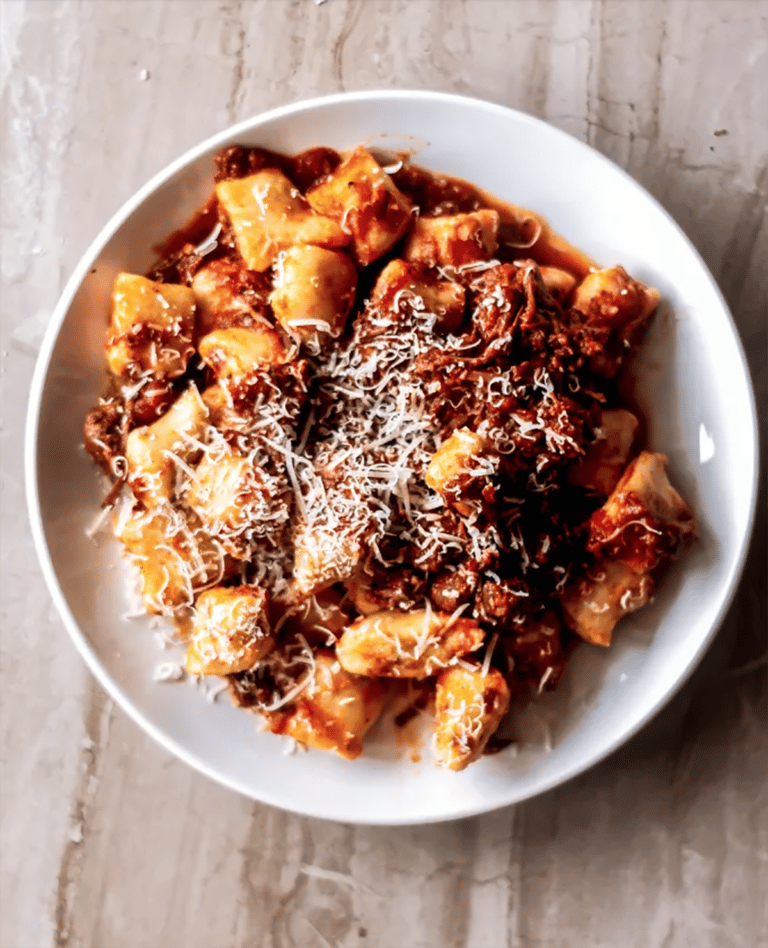 Gnocchi and ragu sauce in a shallow white bowl.
