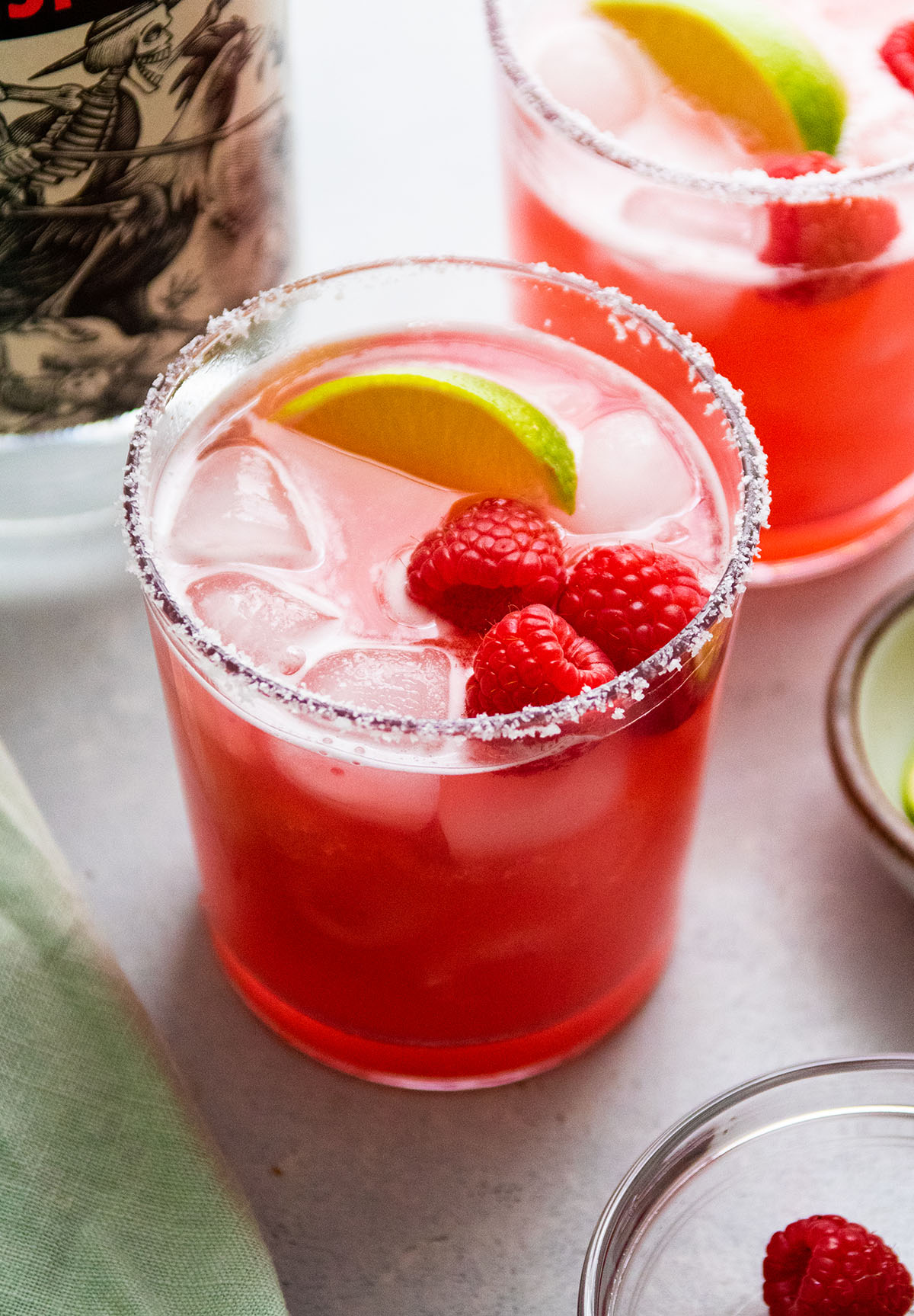 Two raspberry margaritas in short cocktail glasses, in front of a bottle of tequila.