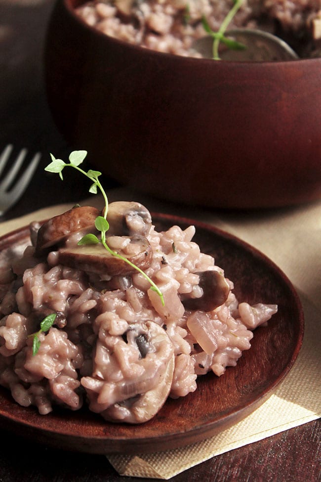 Red wine risotto on a dark wooden plate, topped with a sprig of fresh thyme.
