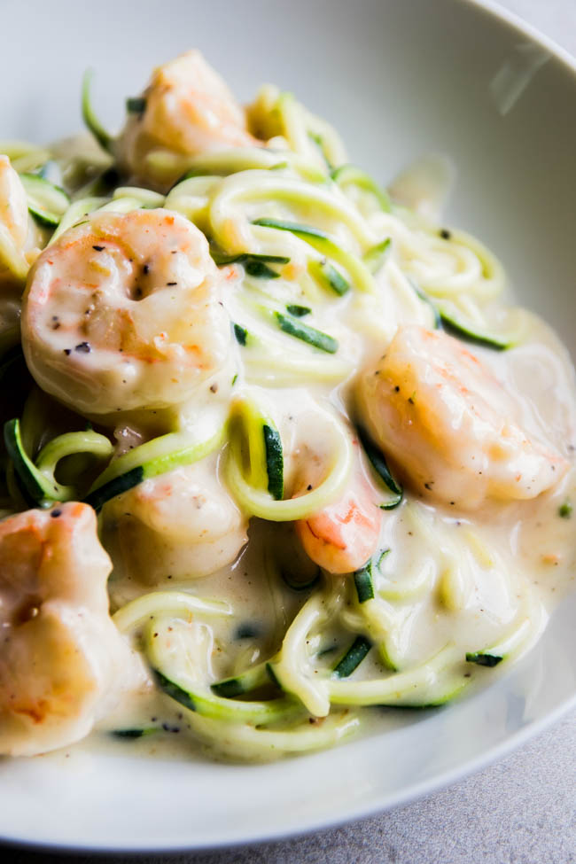 Zucchini noodles and cooked shrimp with white cream sauce in a shallow bowl.
