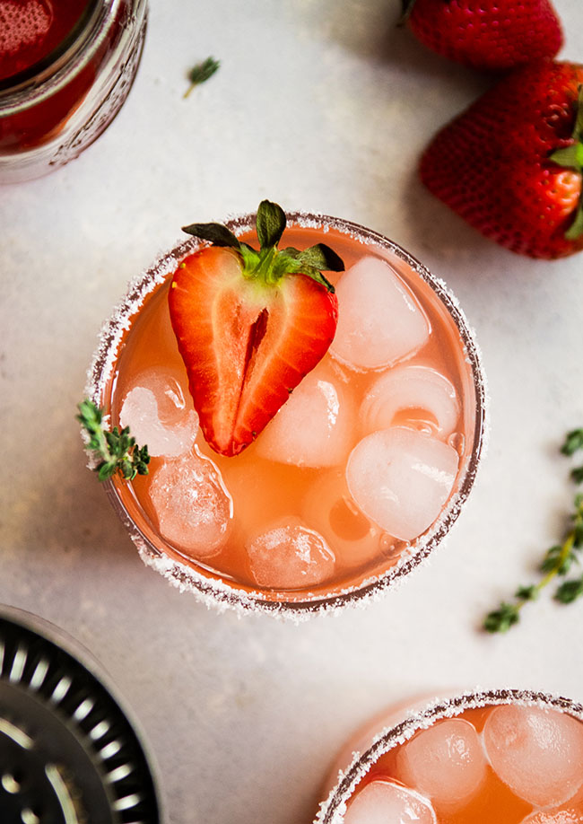 Overhead view of a strawberry cocktail in a glass with salt on the rim and half of a fresh strawberry on top.