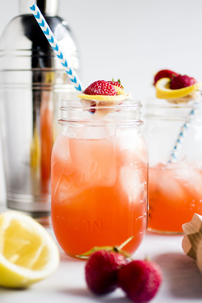 Mason jars filled with strawberry whiskey lemonade in front of a silver cocktail shaker.