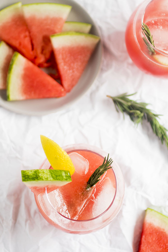 Overhead view of watermelon cocktails on a white table next to a plate of watermelon slices.